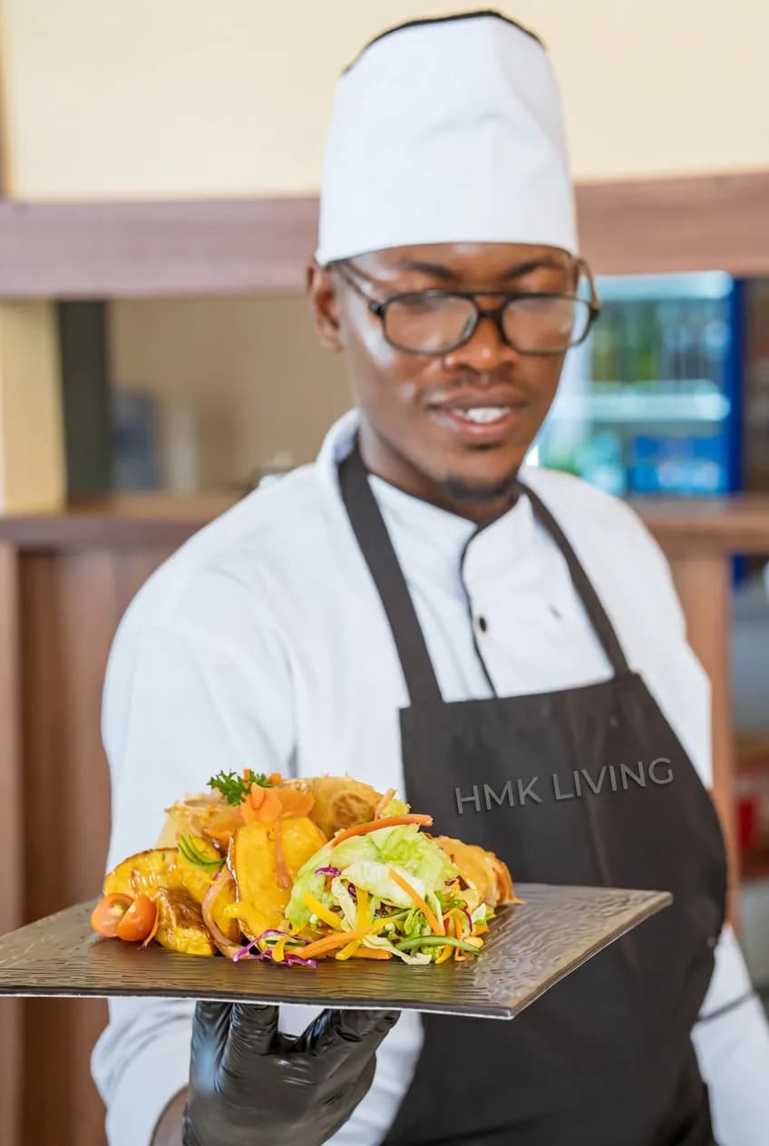An HMK Living chef carrying a plated dish, Kigo Kampala